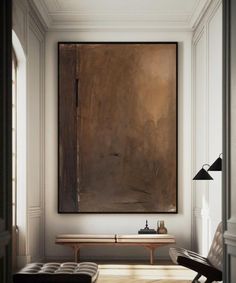 a painting hanging on the wall above a bench in a room with white walls and wooden flooring