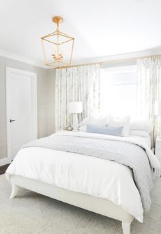 a white bed sitting in a bedroom next to a window with curtains on the windowsill