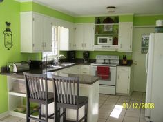 a kitchen with green walls and white cabinets, two bar stools at the island