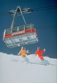 two people riding skis on top of a snow covered slope under a ski lift