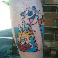 a cartoon tattoo on the leg of a person with an orange and black cat in front of him