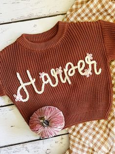 a red sweater with the word harper written on it and a pink flower laying next to it