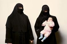 two women in burkas are holding a baby and looking at the camera while standing next to each other