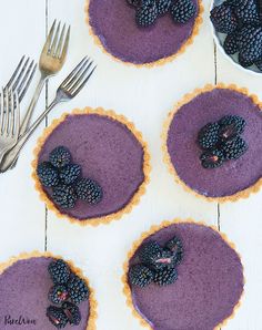 four pies with blueberries and blackberries in them on a white wooden table