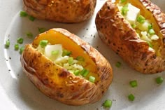 three baked potatoes with cheese and green onions on a white plate, ready to be eaten