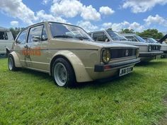 an old car parked in the grass with other cars behind it and people standing around