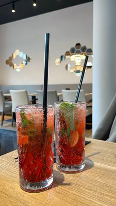 two glasses filled with drinks sitting on top of a wooden table next to each other