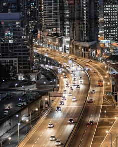 an aerial view of a city at night with cars driving on the road and buildings in the background