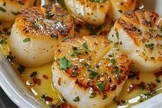 some scallops are in a white dish with sauce and garnishes