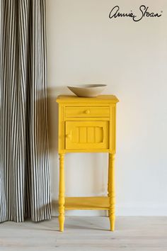 a yellow table with a bowl on top of it in front of a striped curtain