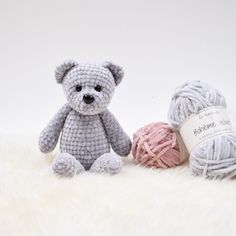 a crocheted teddy bear next to two balls of yarn on a white surface