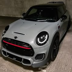 the front end of a silver mini cooper hatchback parked in a parking garage next to a wall