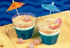 two glasses filled with sand and umbrellas on top of a table