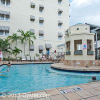 an outdoor swimming pool surrounded by palm trees and people in the background, with apartment buildings on either side