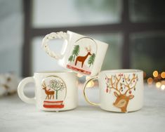 three coffee mugs decorated with deer and christmas trees on them, sitting next to each other