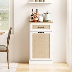 a white cabinet with baskets and bottles on top in a room next to a window