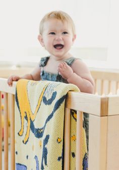 a smiling baby in a crib with a blanket on it's back and his mouth open