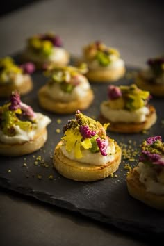 small appetizers with various toppings are arranged on a black tray, ready to be eaten