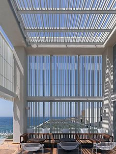 an outdoor dining area with large windows and wooden flooring next to the ocean in front of it