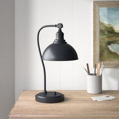 a desk lamp sitting on top of a wooden table next to a cup and pencils