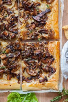 a square pizza with mushrooms and cheese on it next to some bread sticks, lettuce and other food items