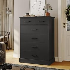 a black chest of drawers sitting in a living room next to a chair and lamp