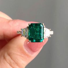 an emerald and diamond ring in someone's hand