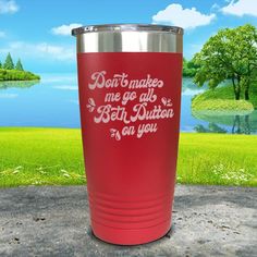 a red tumbler sitting on top of a cement ground next to a lake and trees