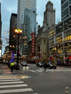 a busy city street with tall buildings in the background at dusk, and traffic lights on both sides