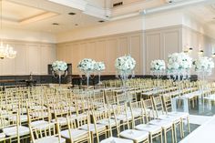 rows of gold chairs with white flowers in vases on each side and chandeliers hanging from the ceiling