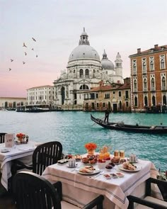 an outdoor dining area with tables and chairs on the water in front of a gondola