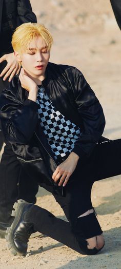 a young man sitting on the ground wearing a black and white checkered neck tie