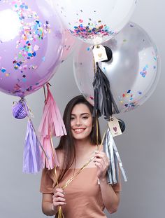 a woman holding up balloons and tassels in front of her face while smiling at the camera