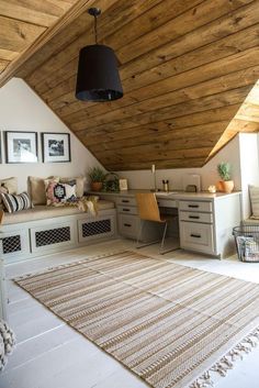 a room with a rug, desk and chair in it under a wooden ceiling that has two framed pictures on the wall