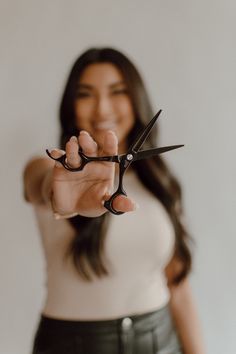 a woman holding scissors in front of her face and pointing at the camera with both hands