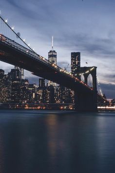 the city skyline is lit up at night as seen from across the water with a bridge in the foreground