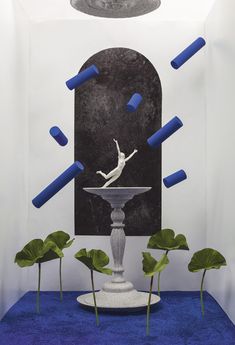 a white statue sitting on top of a blue floor next to green plants and leaves