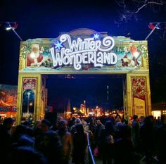 the entrance to winter wonderland at night with people walking under it and onlookers