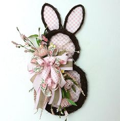 an easter bunny wreath hanging on the wall with pink and white flowers in front of it