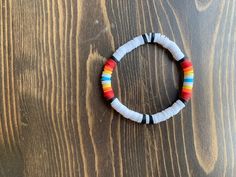 a bracelet with multicolored beads sitting on top of a wooden table in front of a wood wall