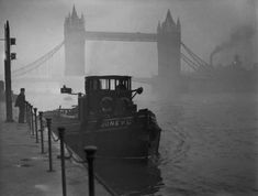 a black and white photo of a tug boat in the water near a bridge on a foggy day