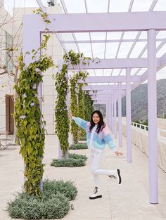 a woman is jumping in the air next to some bushes and plants on a walkway