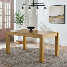 a dining room table with an area rug on the floor next to it and a potted plant