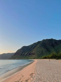 a person walking on the beach with mountains in the background