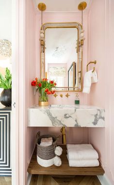 a bathroom with pink walls and marble counter top, gold mirror over the sink and towel rack