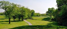 a golf course surrounded by trees and green grass with a dirt path going through it