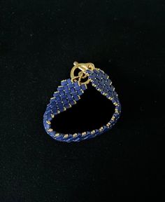 a blue and gold beaded bracelet on a black surface with a golden ring hanging from the clasp