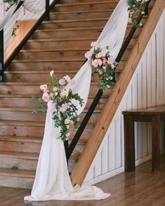 the bride is walking down the stairs in her wedding dress with flowers and greenery