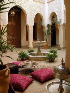 an indoor courtyard with potted plants and decorative seating on the floor, surrounded by arches