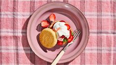 strawberry shortcakes with whipped cream and strawberries on a pink plate next to a fork